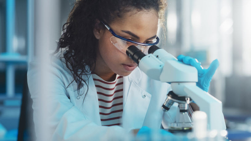 young Black woman looking through a microscope for research young Black woman looking through a microscope for research